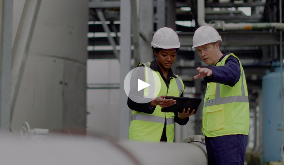 one male, one female engineer in hard hats at factory looking at tablet